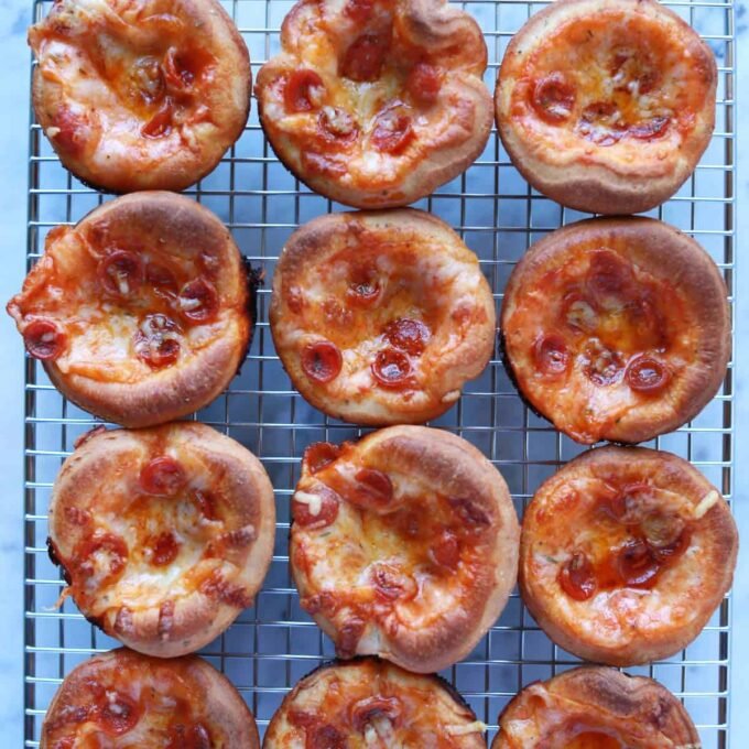 A tray of freshly baked mini pizza cupcakes with melted cheese and pepperoni, garnished with Italian seasoning.