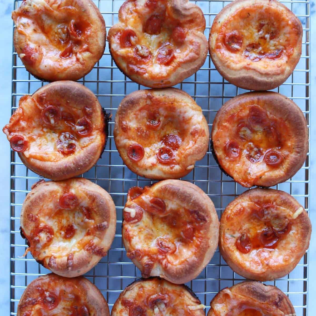 A tray of freshly baked mini pizza cupcakes with melted cheese and pepperoni, garnished with Italian seasoning.