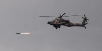 Un hélicoptère de combat Apache israélien tirant un missile vers une cible au Liban, près de la frontière, sur fond de ciel clair.