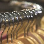 Une femme, visiblement perplexe, essayant un jean dans une cabine d'essayage, avec plusieurs autres vêtements de différentes tailles et marques autour d'elle, symbolisant la confusion des tailles non standardisées.