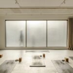 Interior view of Basic Space yoga studio reception area with frosted glass blocks, sculptural check-in desk, and natural light.