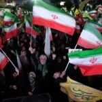 محادثات إيران والولايات المتحدة: توتر متصاعد ودعوات للمقاومة بعد فشل المفاوضات 3 متظاهرون مؤيدون للحكومة الإيرانية يلوحون بالأعلام في طهران، مع لافتة تشير إلى إغلاق مضيق هرمز.