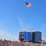 مظلي معلق على شاشة عرض ضخمة في ملعب لين، مع وجود فرق الإنقاذ