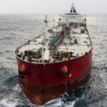 صورة لناقلة نفط ضخمة تعبر مضيق هرمز، مع خلفية لمياه الخليج والسواحل الجبلية.