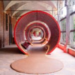 An immersive red architectural installation made from stacked Mutti tomato pulp cans at the Università degli Studi di Milano during Milan Design Week, showcasing ephemeral and circular design.
