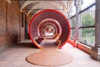 An immersive red architectural installation made from stacked Mutti tomato pulp cans at the Università degli Studi di Milano during Milan Design Week, showcasing ephemeral and circular design.