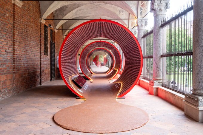 An immersive red architectural installation made from stacked Mutti tomato pulp cans at the Università degli Studi di Milano during Milan Design Week, showcasing ephemeral and circular design.