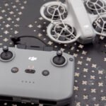 Un drone DJI Neo blanc avec ses accessoires (casque FPV, télécommande, batteries) posés sur une surface sombre, avec un fond flou.