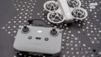 Un drone DJI Neo blanc avec ses accessoires (casque FPV, télécommande, batteries) posés sur une surface sombre, avec un fond flou.