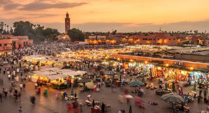 Vue aérienne d'une plage marocaine ensoleillée avec des touristes profitant du sable fin et de la mer turquoise, symbolisant l'essor du secteur touristique.