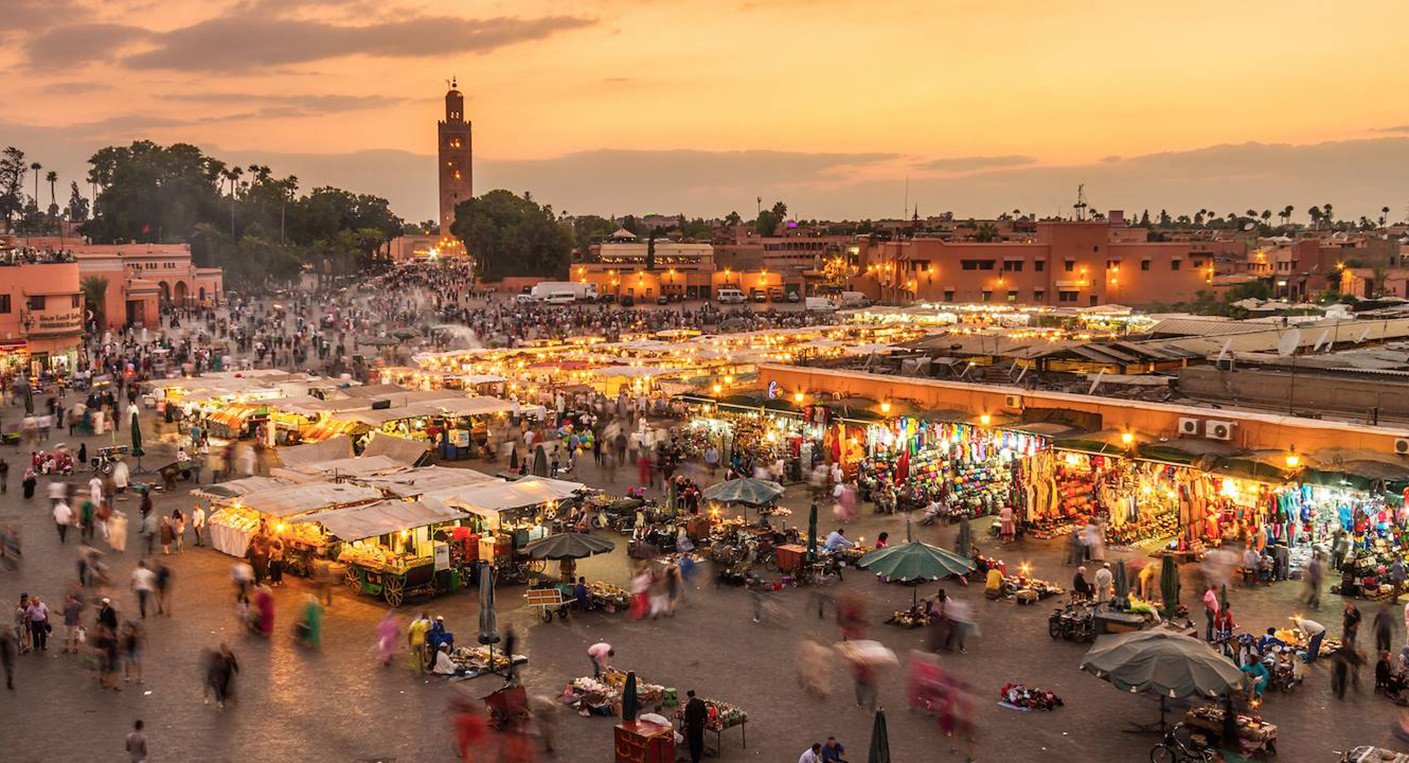 Vue aérienne d'une plage marocaine ensoleillée avec des touristes profitant du sable fin et de la mer turquoise, symbolisant l'essor du secteur touristique.