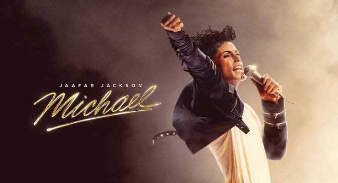 Jaafar Jackson dans le rôle de Michael Jackson, recréant une pose emblématique sur scène, avec un éclairage dramatique et une foule en arrière-plan.