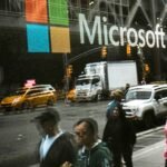A reflection of people on a Microsoft store in Manhattan, symbolizing workforce and corporate presence.