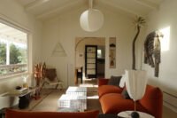 A vibrant living room in a Silver Lake bungalow featuring a burnt orange velvet sofa, chrome accents, and eclectic decor, showcasing a blend of vintage and modern design.