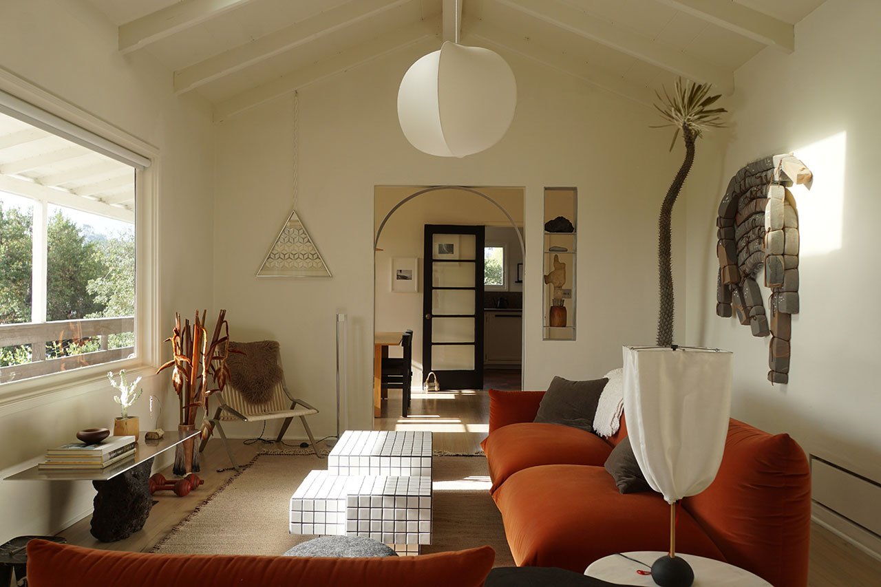A vibrant living room in a Silver Lake bungalow featuring a burnt orange velvet sofa, chrome accents, and eclectic decor, showcasing a blend of vintage and modern design.