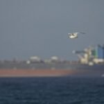 A large commercial oil tanker navigating the narrow waters of the Strait of Hormuz with land visible on either side.