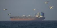 A large commercial oil tanker navigating the narrow waters of the Strait of Hormuz with land visible on either side.