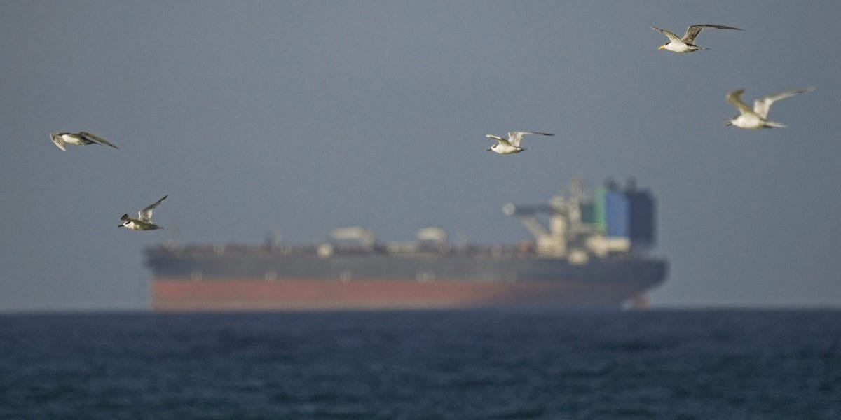 A large commercial oil tanker navigating the narrow waters of the Strait of Hormuz with land visible on either side.