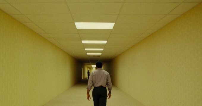 Kane Parsons, director of The Backrooms movie, standing in a dimly lit, mono-yellow hallway reminiscent of the Backrooms aesthetic.