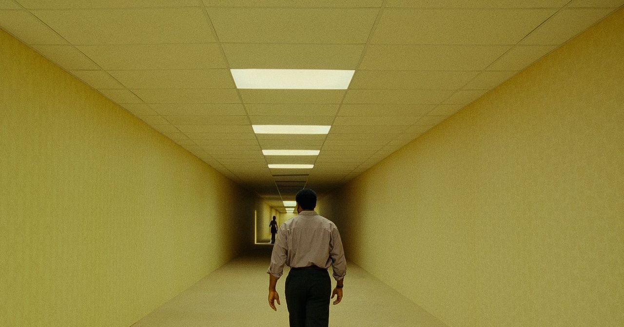 Kane Parsons, director of The Backrooms movie, standing in a dimly lit, mono-yellow hallway reminiscent of the Backrooms aesthetic.