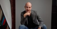 Cecil Baldwin, host of Welcome to Night Vale, in a professional portrait, perhaps with his signature 'dope boots'.