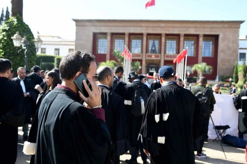 Un groupe d'avocats en robe noire manifestant devant un tribunal au Maroc, symbolisant la crise entre la profession et le ministère de la Justice.