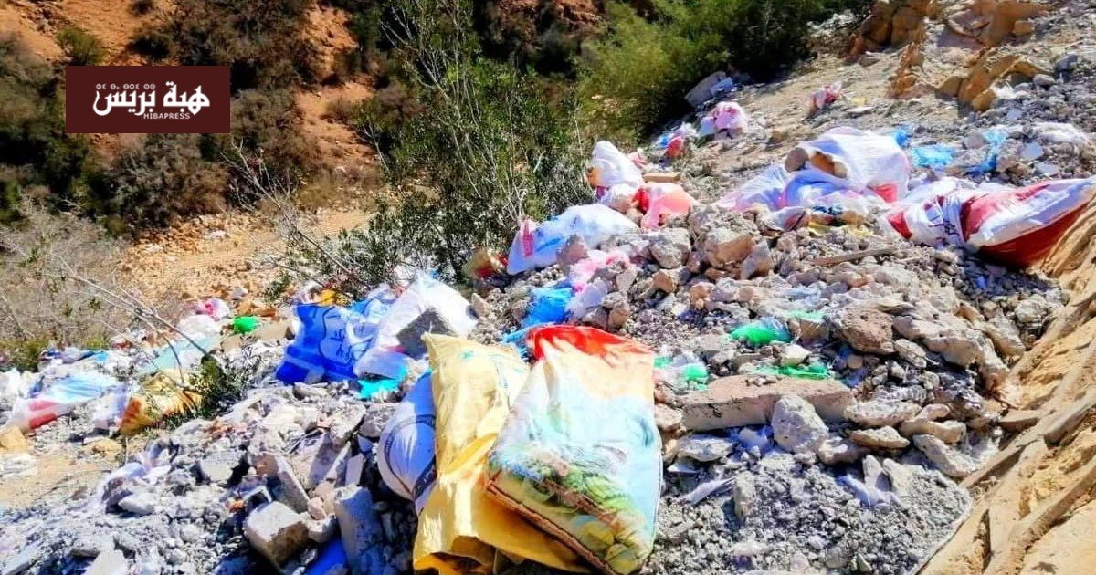 صورة لغابة أغروض مليئة بالنفايات البلاستيكية ومخلفات البناء، مع أشجار أركان متضررة في الخلفية.