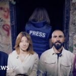 صورة لصحفيين يرتدون سترات واقية تحمل كلمة 'PRESS' وخوذات في منطقة نزاع بجنوب لبنان.