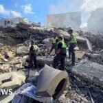 عناصر من الدفاع المدني اللبناني يتفقدون أنقاض مبنى مدمر في منطقة الحوش بجنوب لبنان، قرب مدينة صور، بعد غارة إسرائيلية.