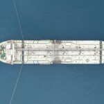 Un pétrolier naviguant dans le détroit d'Ormuz, avec des navires de guerre en arrière-plan, symbolisant les tensions géopolitiques et l'impact sur l'économie.