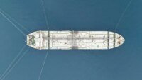 Un pétrolier naviguant dans le détroit d'Ormuz, avec des navires de guerre en arrière-plan, symbolisant les tensions géopolitiques et l'impact sur l'économie.