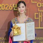 Kim Miso, artiste marocaine de K-pop, vêtue d'un caftan traditionnel marocain, souriant et tenant son prix "Global Entertainment" à Séoul.