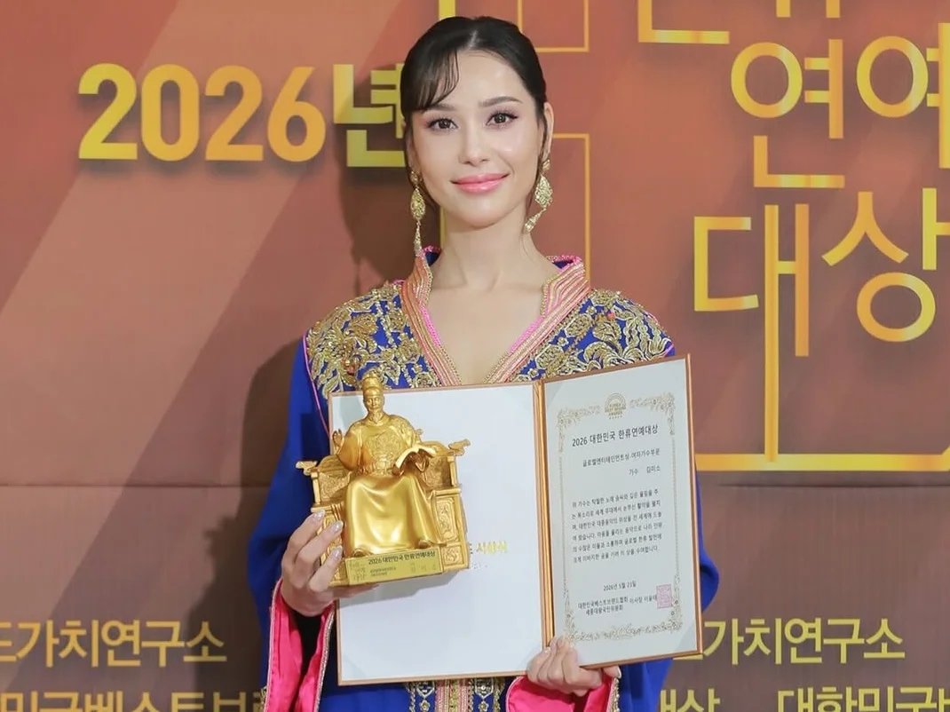 Kim Miso, artiste marocaine de K-pop, vêtue d'un caftan traditionnel marocain, souriant et tenant son prix "Global Entertainment" à Séoul.