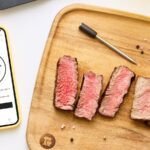 A KitchenAid Smart Thermometer with its probes, displaying temperature readings on a smartphone app.