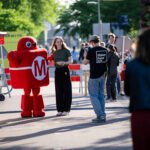 Diverse crowd exploring interactive robotic and artistic installations at Maker Faire Delft on TU Delft campus.