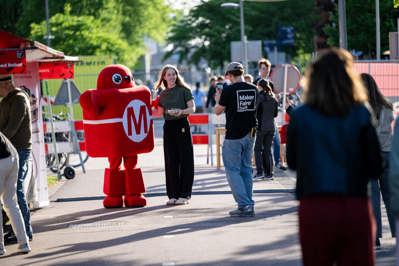 Diverse crowd exploring interactive robotic and artistic installations at Maker Faire Delft on TU Delft campus.