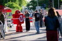 Diverse crowd exploring interactive robotic and artistic installations at Maker Faire Delft on TU Delft campus.