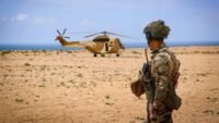Soldats marocains et américains participant à une opération de recherche et de sauvetage sur une côte rocheuse, avec des véhicules militaires et un hélicoptère en arrière-plan.