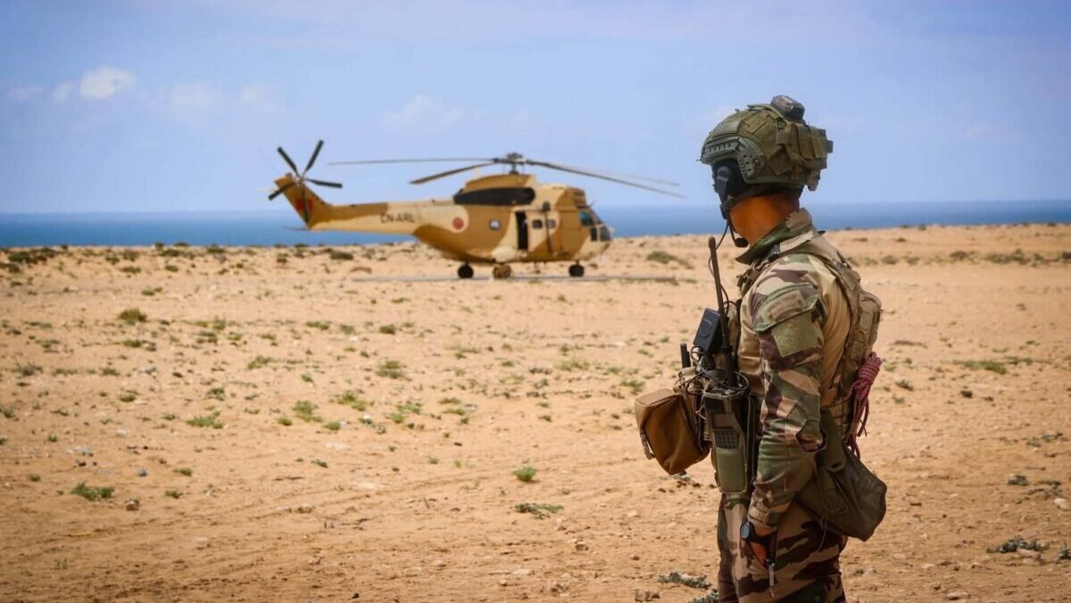 Soldats marocains et américains participant à une opération de recherche et de sauvetage sur une côte rocheuse, avec des véhicules militaires et un hélicoptère en arrière-plan.