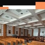 Various luxury seat cushions on hard wooden benches in a courtroom, with legal documents and water bottles nearby.