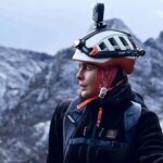Nawal Sfendla, alpiniste marocaine, souriante et équipée pour l'alpinisme, avec un paysage montagneux en arrière-plan, symbolisant sa détermination et son exploit sur l'Everest et le Lhotse.