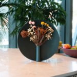 The Nimbus Vase by Ben Peng, a sculptural vessel with a metallic halo-like ring framing flowers, set in a minimalist interior.