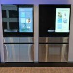 A modern Samsung Bespoke refrigerator with a large touchscreen display showing various smart features and food recognition.