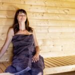 A person relaxing inside a modern wooden sauna, with steam rising and warm lighting.