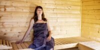 A person relaxing inside a modern wooden sauna, with steam rising and warm lighting.