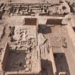 Vue aérienne des fouilles archéologiques de Sijilmassa, montrant les vestiges de la cité médiévale et la structure métallique moderne en construction, évoquant les dunes du désert.