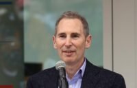 Amazon CEO Andy Jassy speaking, with a subtle AI-themed background.