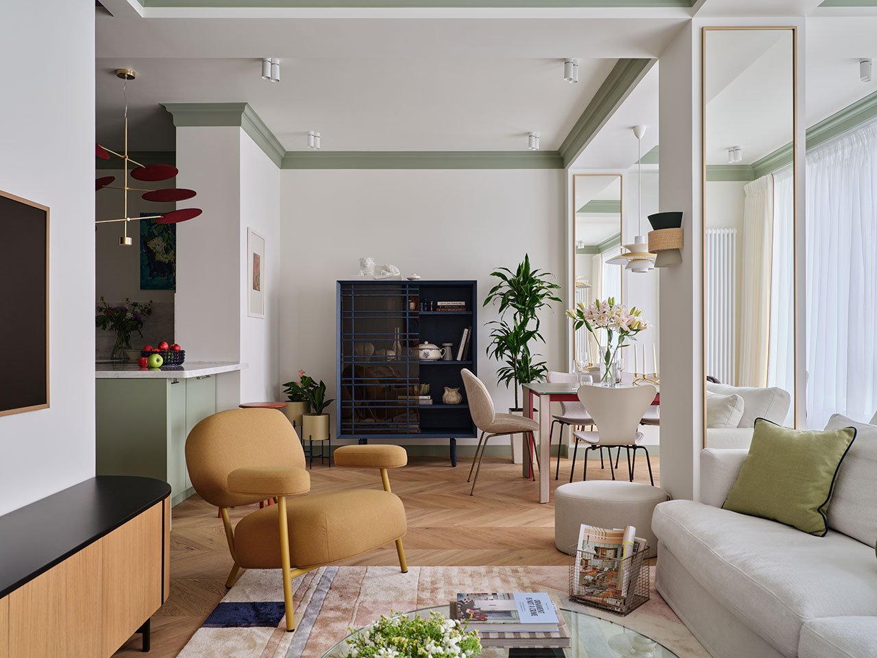 Stylish living room in an Almaty apartment featuring sage walls, mirrored columns, and curated modern furnishings.