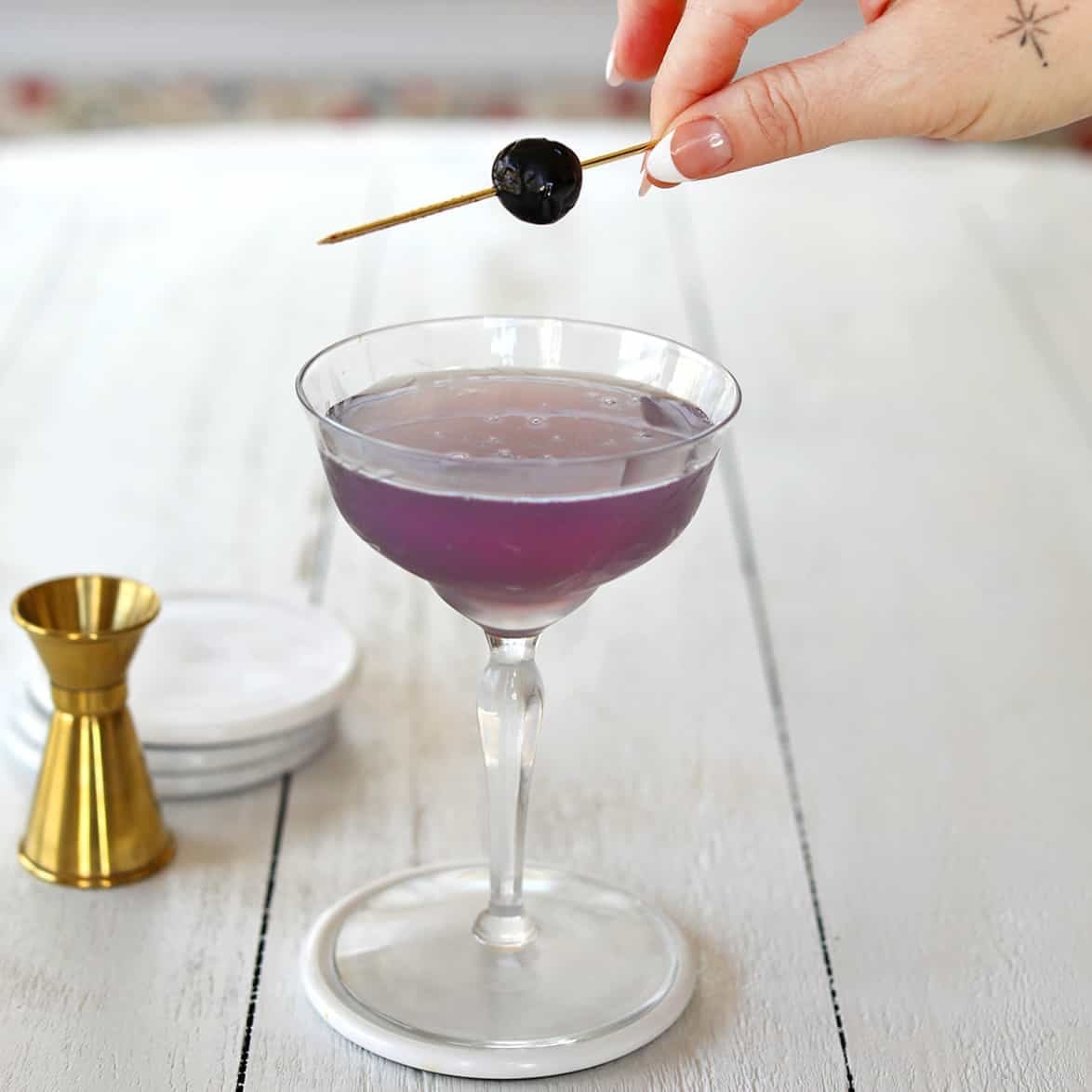 A vibrant purple Aviation cocktail in a coupe glass, garnished with a maraschino cherry and a lemon twist.