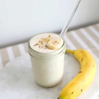 A creamy banana smoothie garnished with a banana slice and a drizzle of honey in a clear glass.